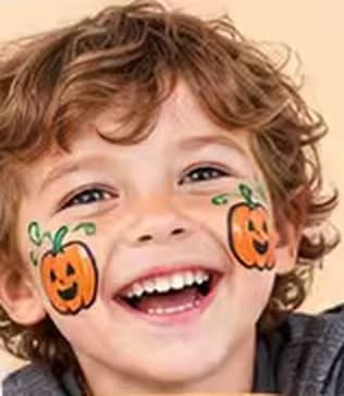 A laughing boy with little pumpkins face-painted on both cheeks